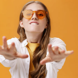 Girl reaching with desire at camera wanting grab it. Portrait of good-looking stylish caucasian young woman in trendy sunglasses biting lip from will to have something pulling hands towards. Body language concept